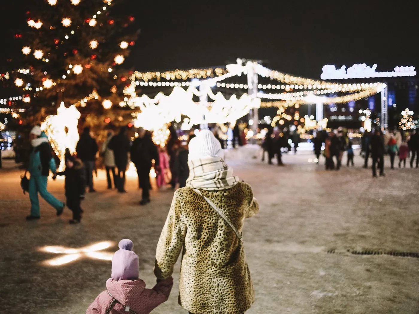 A mother and child walking hand in hand into a holiday lights display